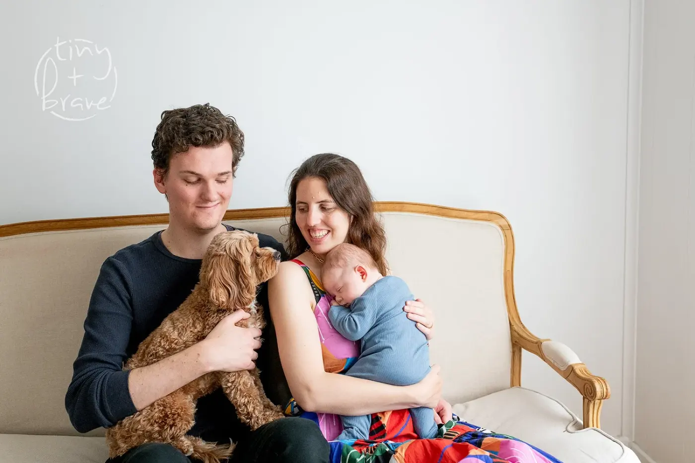 Parents and their newborn on a velvet sofa with the family dog