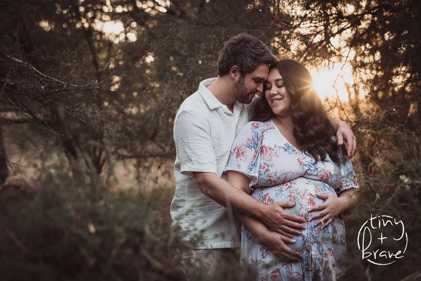 Expecting parents embracing at sunset